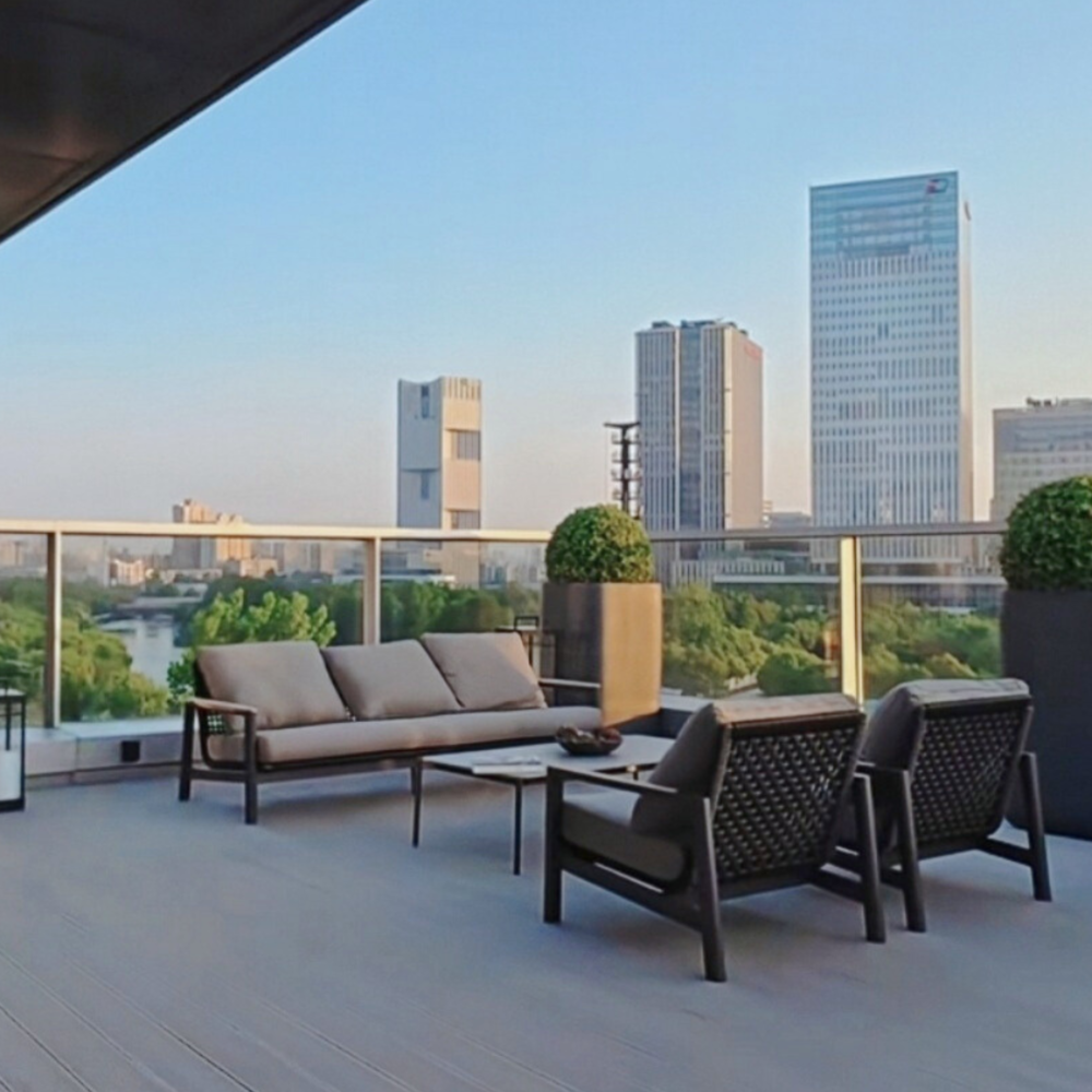 Modern outdoor balcony with charcoal rope lounge set, coffee table, and armchairs overlooking city skyline.