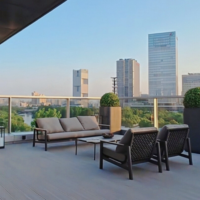 Modern outdoor balcony with charcoal rope lounge set, coffee table, and armchairs overlooking city skyline.